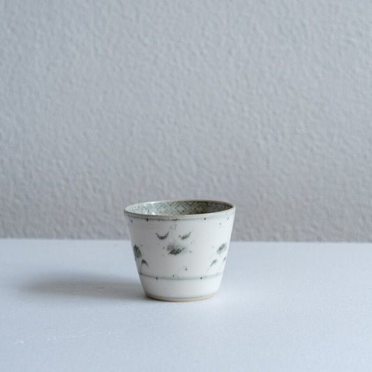Small white porcelain cup with a faintly speckled glaze and sparse blue underglaze markings.