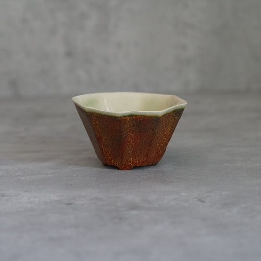 Low faceted cup in mottled rust orange with a pale cream glazed interior.