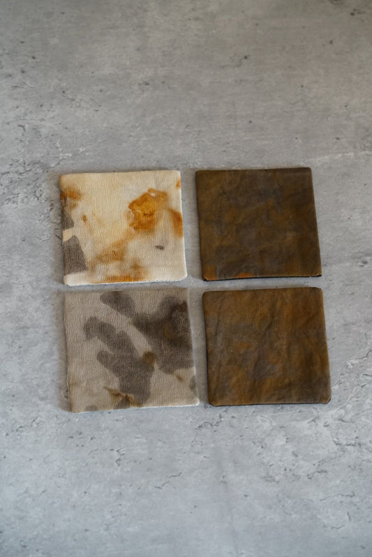 Four small square cloth coasters dyed in iron grey, rust and cream, laid in a block.