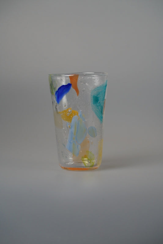 Tall clear glass tumbler splashed with bold patches of blue, yellow and orange.
