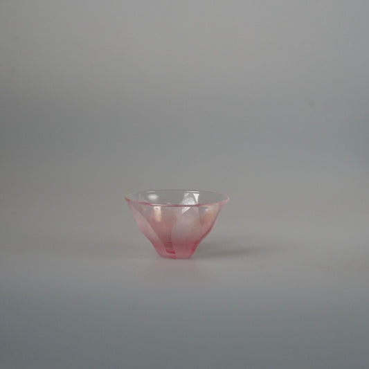 Small flared glass tea cup in soft rose pink with a fine folded rim, on pale grey.