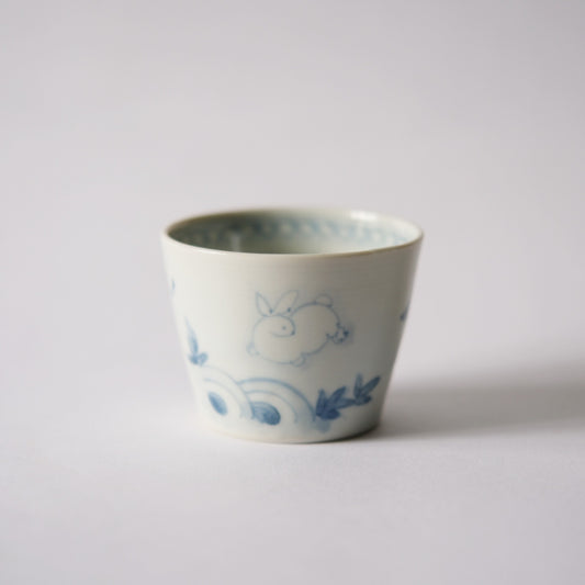 White cup painted in soft blue with a rabbit and scattered leaf shapes.