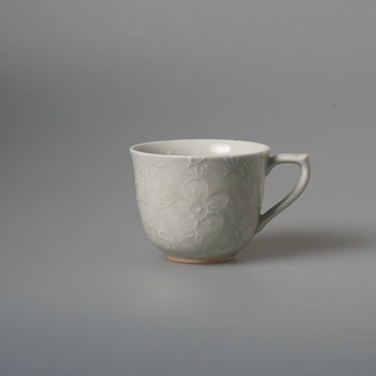 Grey-blue mug carved with faint blossoms, with a slim curved handle, on pale grey.