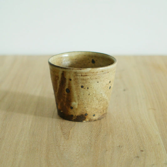 Straight-sided wood-fired cup in speckled cream with a dark scorch running up one side.