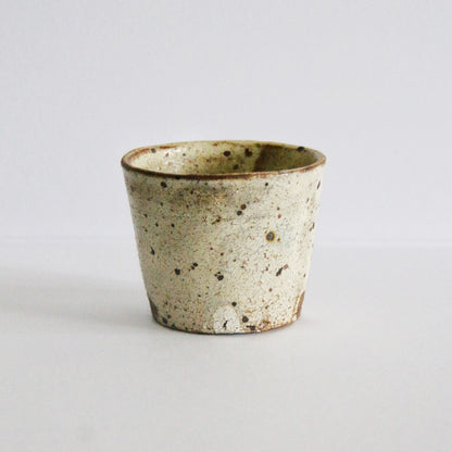 Tapered cream cup heavily flecked with dark iron spots and a thin brown line at the rim.