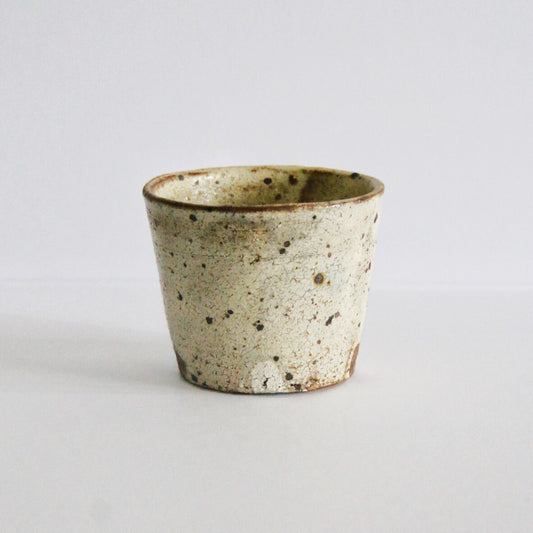 Tapered cream cup heavily flecked with dark iron spots and a thin brown line at the rim.