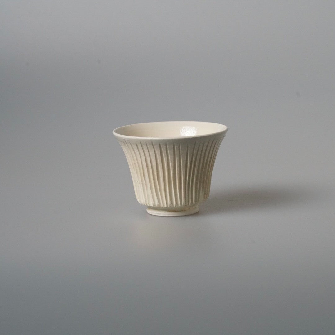 Small cream cup on a low foot, its outer wall carved in close vertical ribs.