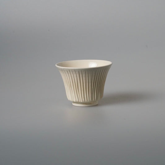 Small cream cup on a low foot, its outer wall carved in close vertical ribs.