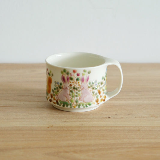 White porcelain mug painted with a soft meadow of small pink and green flowers, on a wooden table.