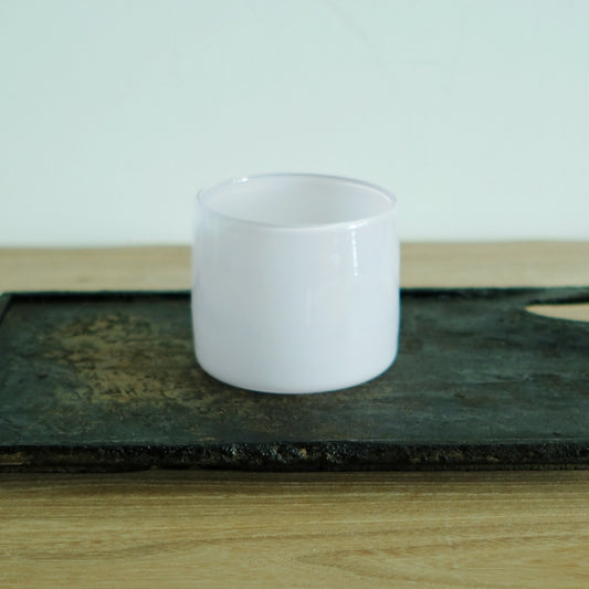 Short opaque milk-white glass cup with straight sides, on a dark weathered board.