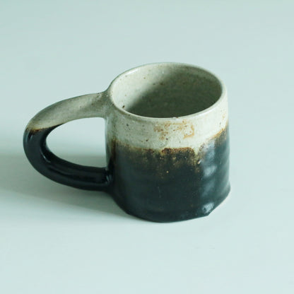 Faceted mug graded from cream at the rim to near black below, with a chunky dark handle.