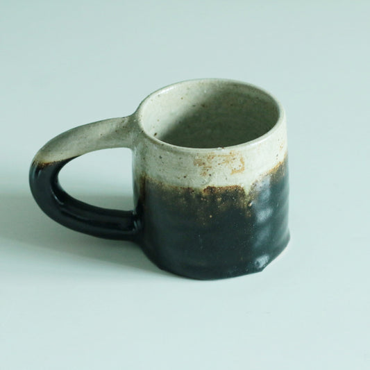 Faceted mug graded from cream at the rim to near black below, with a chunky dark handle.