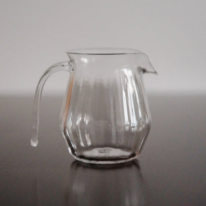 Clear glass jug with softly faceted sides, a drawn lip and a slender applied handle.
