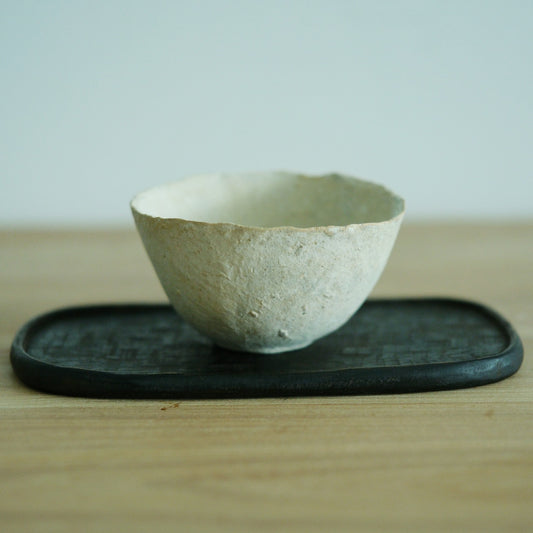 Wide shallow cream cup with a torn, uneven rim and a chalky surface, on a dark tray.