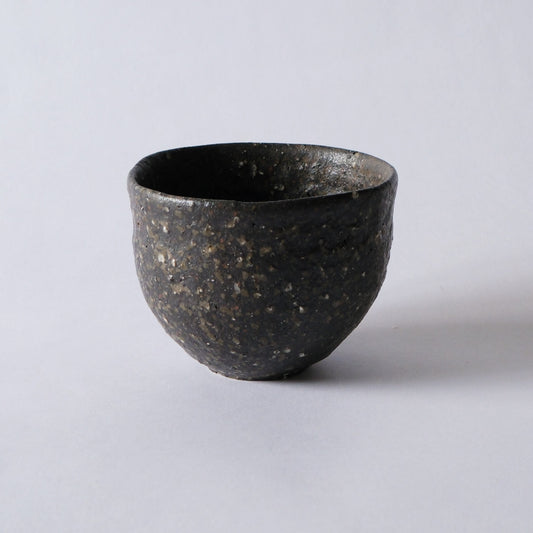 Deep dark cup with a coarse gritty surface flecked with pale specks, lit against white.