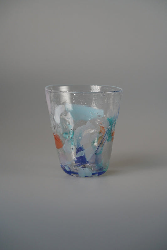 Clear glass tumbler splashed with brushstrokes of blue, turquoise and orange colour.