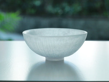 Shallow cast glass bowl in frosted white with a faint blue cast, glowing against a bright window.