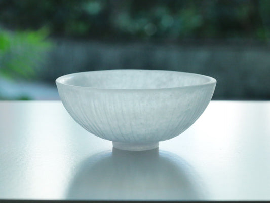 Shallow cast glass bowl in frosted white with a faint blue cast, glowing against a bright window.