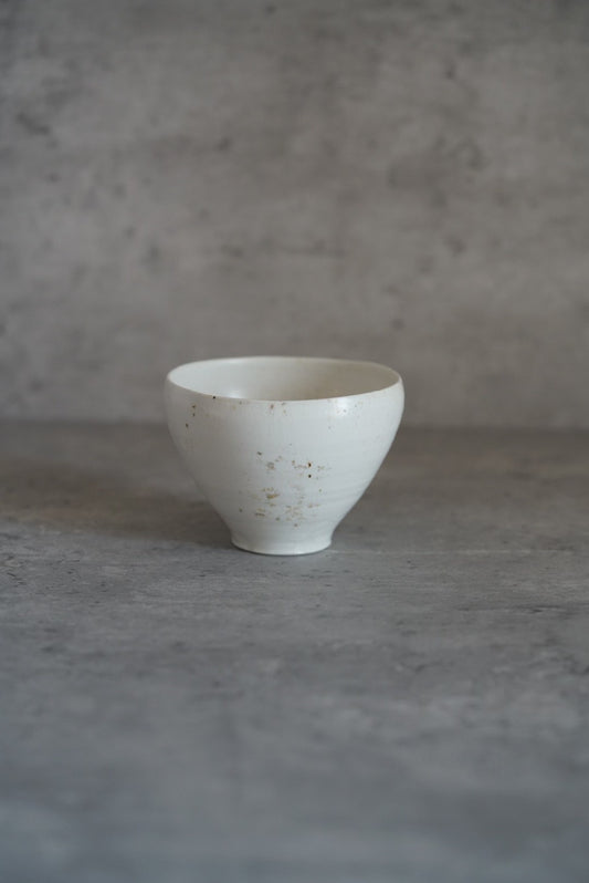 White porcelain tea bowl on a small foot, its walls flaring to a fine speckled rim.