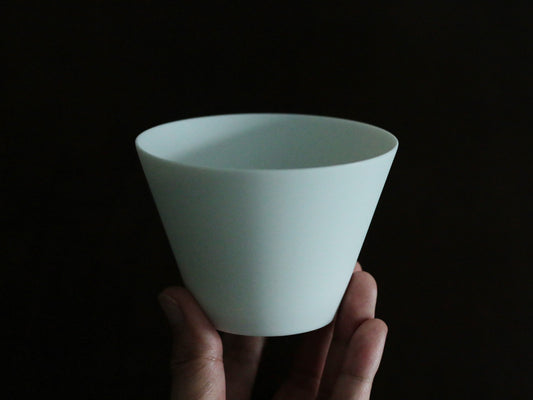 Conical white porcelain cup with very thin walls, held in a hand against a black background.