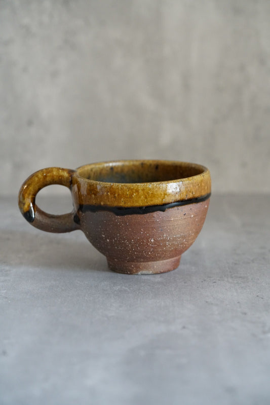 Wide mug with a golden amber glazed rim over a rough brown body, with a ring handle.