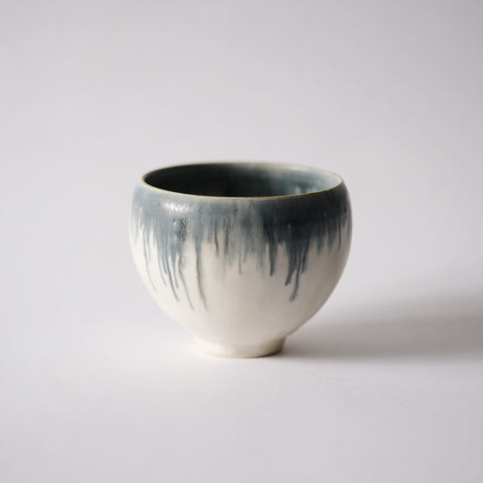 White footed bowl with dark grey glaze running down from the rim in long uneven drips.