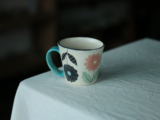 White mug with a turquoise handle, painted with a large pink bloom and dark blue leaves.