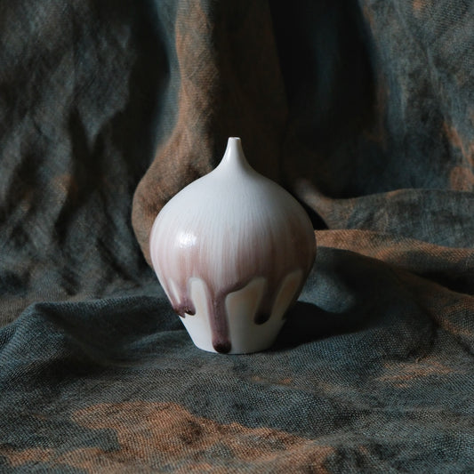 Small bulb-shaped vase with a narrow neck, glazed white over soft pink and brown drips, on dark cloth.