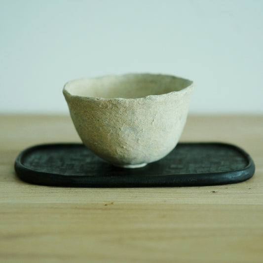 Wide cream cup with a chalky, sandy surface and a softly uneven rim, on a dark tray.