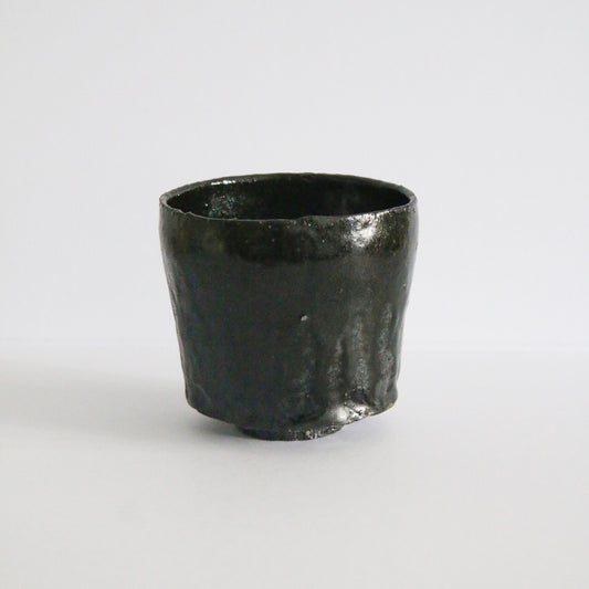 Deep tea bowl in glossy black glaze with a softly uneven rim and warm brown breaking at the edge.