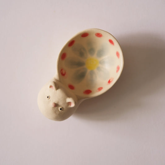 Cream ceramic scoop painted with red dots and a yellow flower, its handle modelled as a small animal.