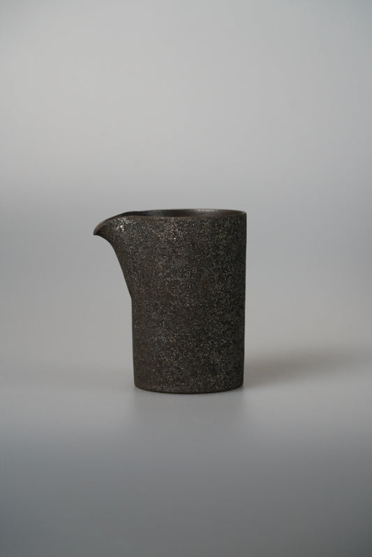 Tall dark pouring vessel in gritty metallic glaze with a small drawn lip.