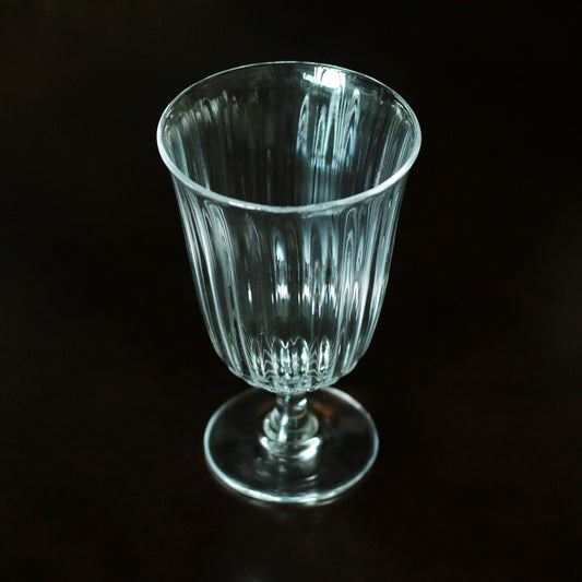 Tall stemmed glass with fine vertical ribbing and a pale green cast, lit against black.