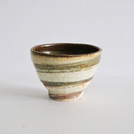 Small footed cup banded in cream, rust and olive slip, with a dark glazed rim.