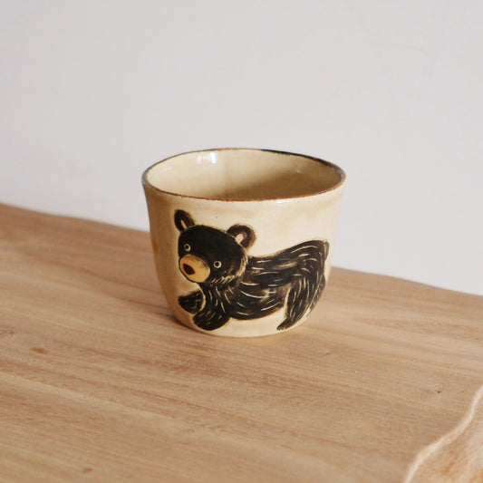 Cream cup with a brown rim, painted with a black bear stretched right around its side.