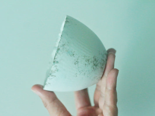 Shallow mint green cup held in a hand, its glaze pooling darker towards the centre.