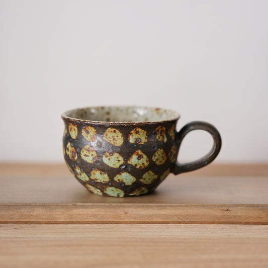 Dark mug ringed with pale green spots and a loop handle, on a light wooden shelf.