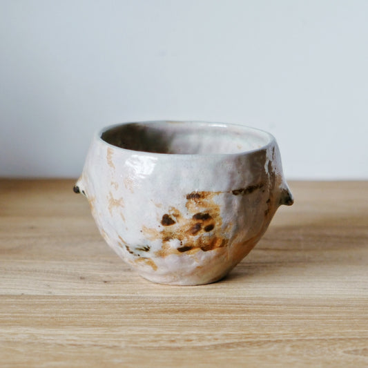 Rough hand-built cup in crusty white with rust-brown scorch marks and an uneven torn rim.