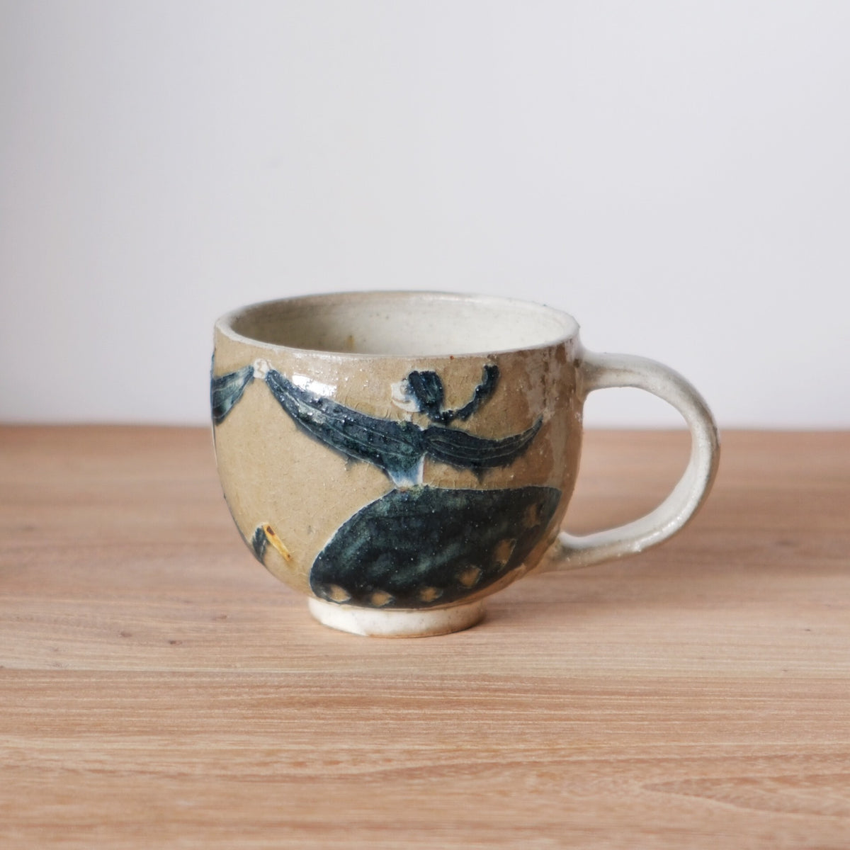 Cream ceramic mug with a chunky handle, painted with bold navy leaves and small dots.