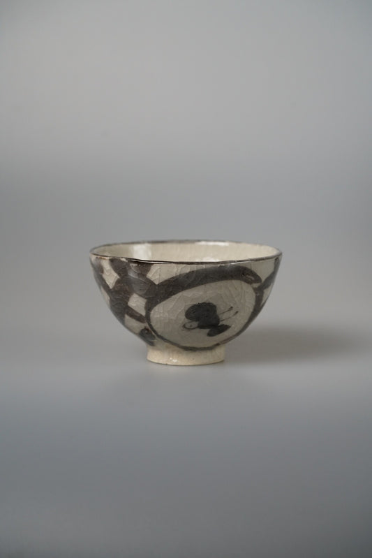 Cream bowl painted with bold black brush marks and a soft round shape at its side.