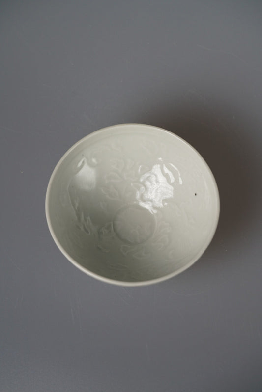 Shallow celadon bowl seen from above, its faint carved pattern showing beneath the glaze.