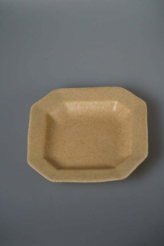 Octagonal plate in speckled ochre with a wide flat rim, seen from above on grey.