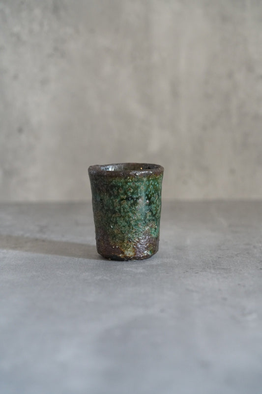 Small straight-sided cup in mottled green and rust glaze, on a pale grey ground.