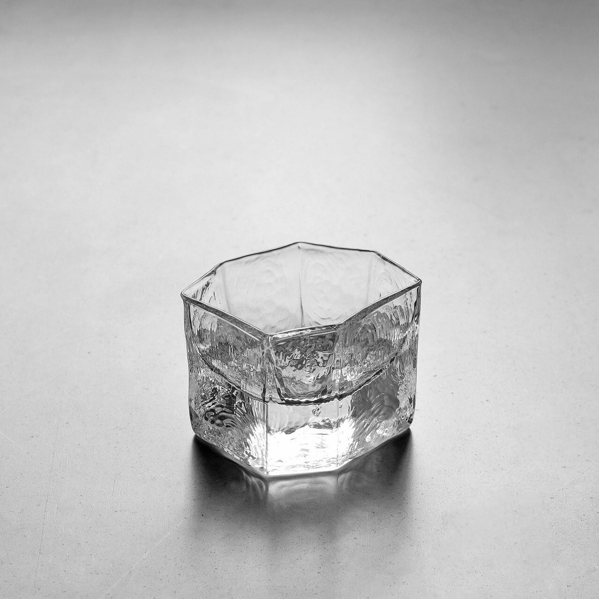 Small hexagonal clear glass cup with thick faceted walls and a rippled surface.
