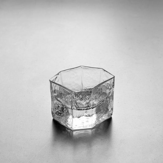 Small hexagonal clear glass cup with thick faceted walls and a rippled surface.