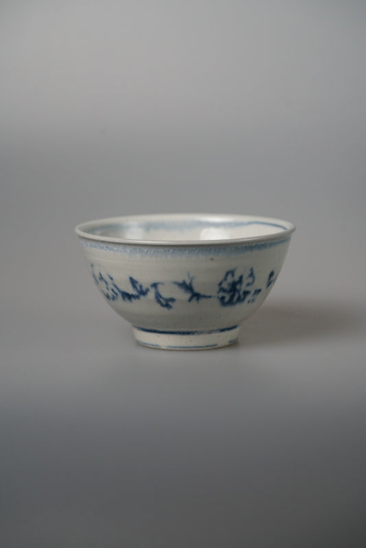 Footed white bowl painted with a band of fine blue flowering vines below the rim.