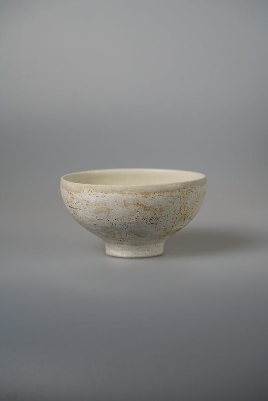 Footed bowl in speckled cream with rust flecks and a pale glazed interior.