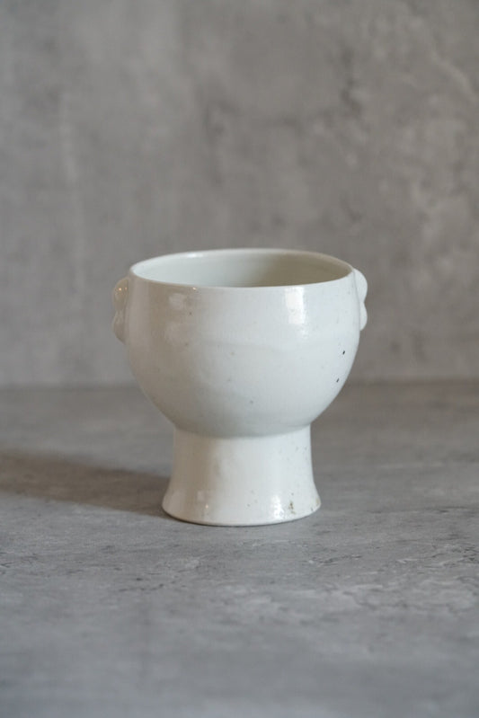 Tall white footed cup with small lugs at the rim, standing on a pale grey ground.
