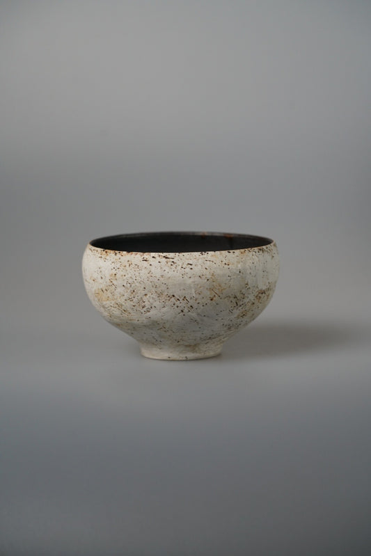 Footed cream bowl speckled with iron, its interior glazed deep black.