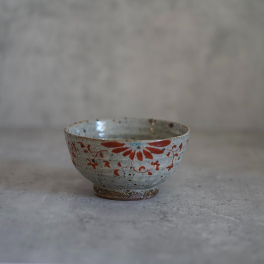 Footed bowl painted in red and blue with radiating flower motifs across a speckled white ground.